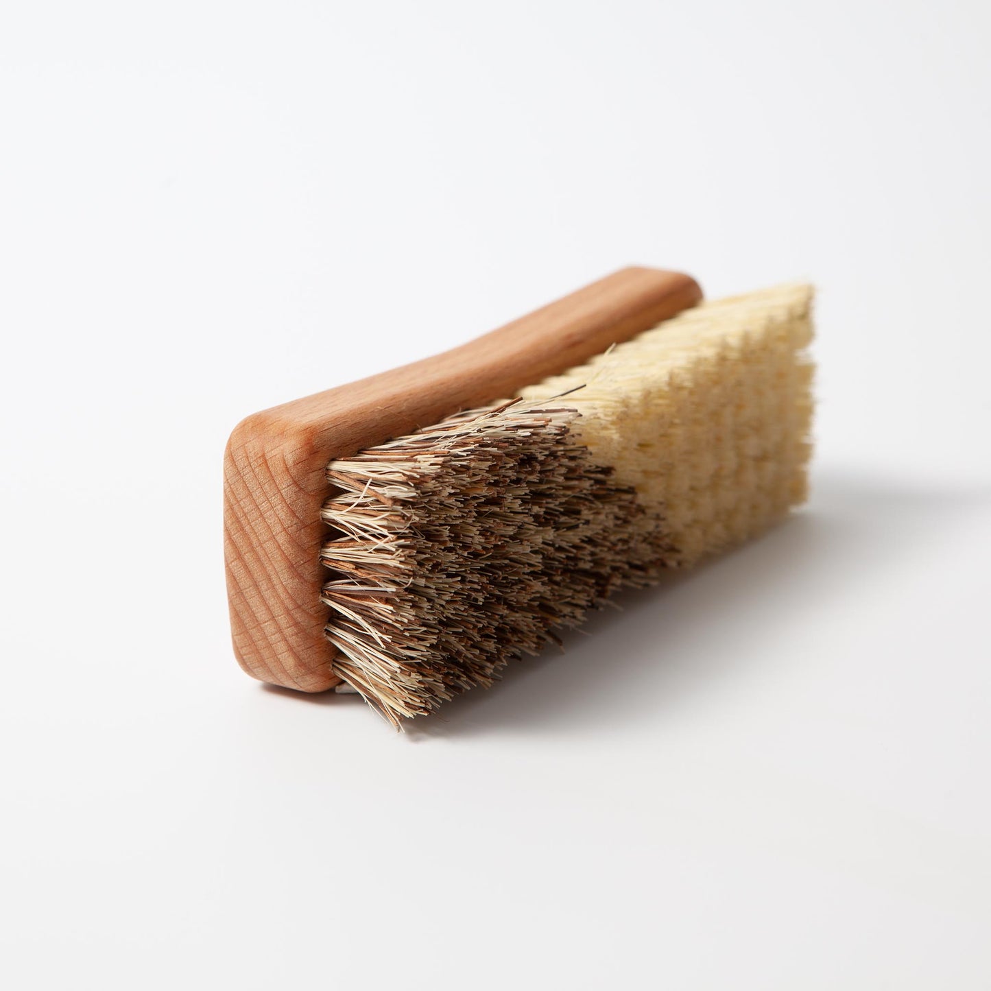 Auf der Seite liegendes Produktfoto der Cappall-Wurzelbürste vor weißem Hintergrund. Die Wurzelbürste für Pferde wurde so platziert, dass die pflanzlichen Borsten in zwei Farben (gelblich und bräunlich) besonders gut sichtbar sind.